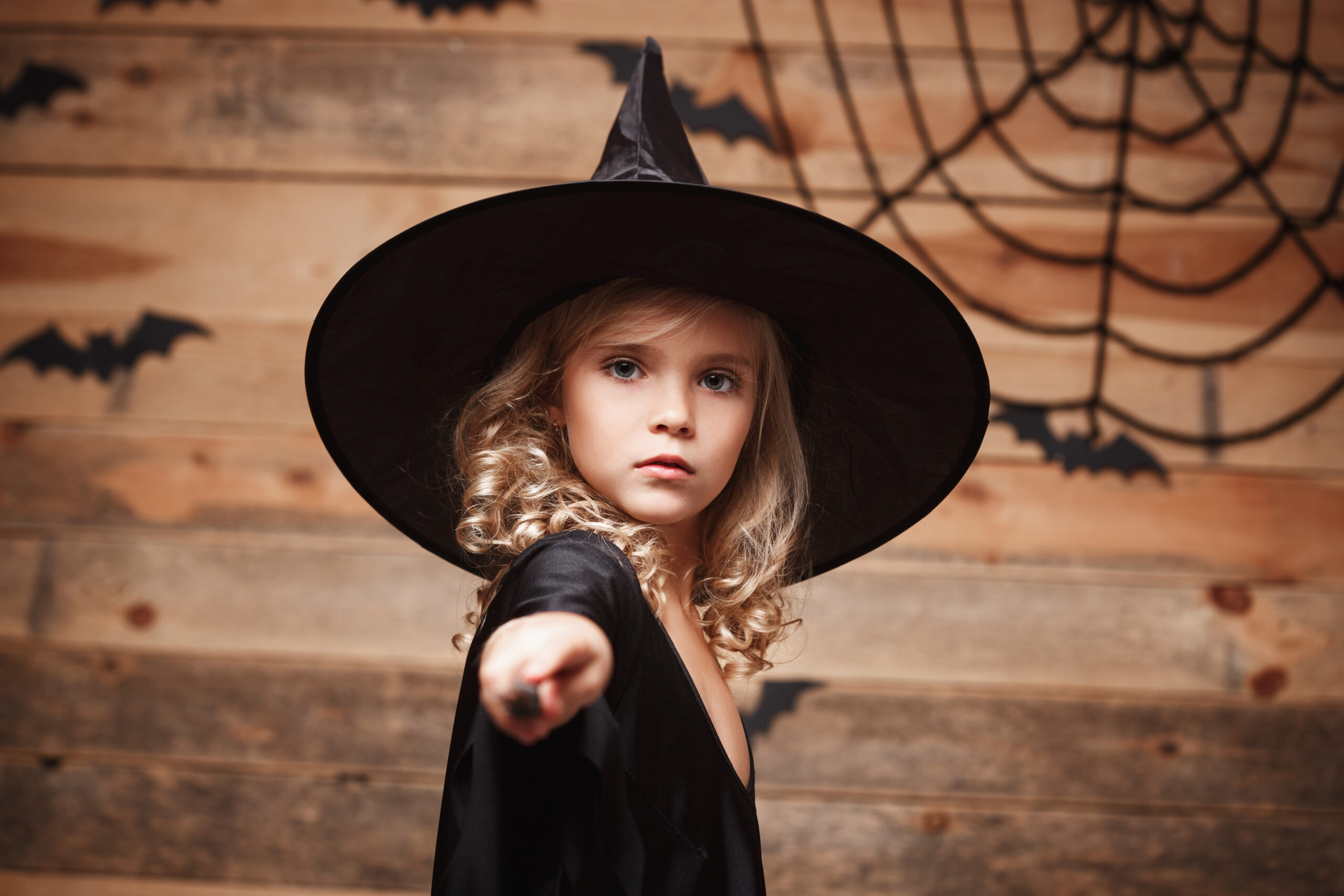 Halloween Witch concept - little witch child enjoy playing with magic wand. over bat and spider web background