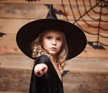 Halloween Witch concept - little witch child enjoy playing with magic wand. over bat and spider web background