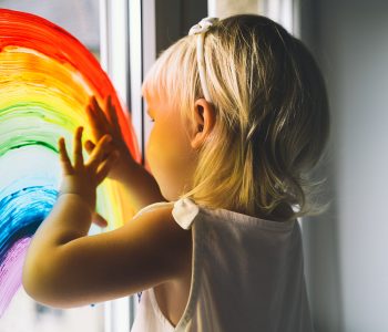 Little girl hands touch painting rainbow on window. Child Art and Creative. Kids leisure at home, childcare, safety joy symbol. Positive visual support during quarantine Coronavirus Covid-19 at home.