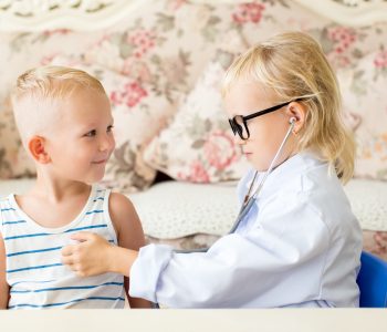 Portrait of serious little girl playing doctor examining boy patient with stethoscope. Occupation, health and childhood concept